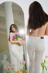 brunette topless at the mirror in a room with bouquets of tulips on the floor