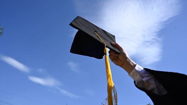 Close-up of a woman's hand with a graduation cap against the blue sky. 