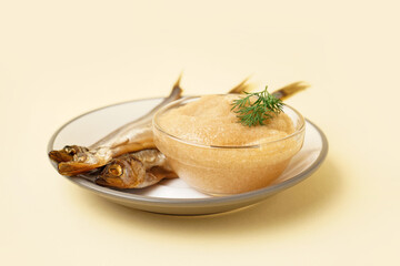 Plate with bowl of caviar and smoked capelin fishes on beige background