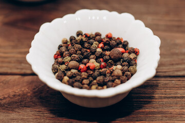 Black, fragrant, red pepper spices in bowls on a wooden table.