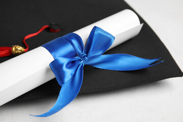 Diploma with blue ribbon and graduation hat on white table