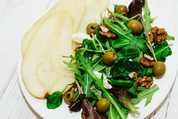 Salad with pears, herbs, arugula, prosciutto, cheese, green olives and nuts.