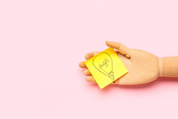 Wooden hand and sticky paper with drawn light bulb on pink background