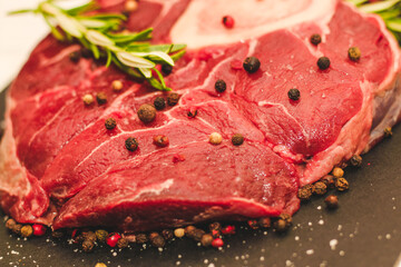 Fresh piece of meat large beef steak on the bone ossobuco with a sprig of rosemary on a black background.