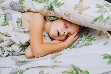 A beautiful girl, a five-year-old preschool child, is fast asleep on a bed, on a pillow, covered...