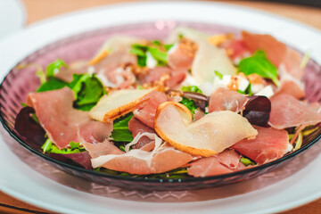 Salad with herbs, arugula, prosciutto, cheese, green olives and nuts.