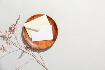 Wooden plate with blank card, envelope and dried flowers on grey background