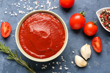 Bowl of tasty tomato paste, rosemary, peppercorn and garlic cloves on blue grunge background