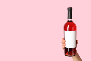 Female hand holding bottle of red wine on pink background