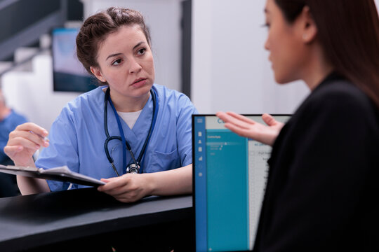 Medical assistant showing patient expertise to receptionist while asking her to programming another examination. Medical staff working in hospital waiting area, health care service support