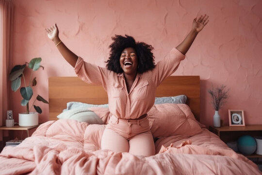 Ecstatic joyful Black curvy woman dressed in pink in bedroom laughing. 