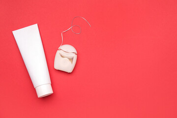 Dental floss and tube of toothpaste on red background