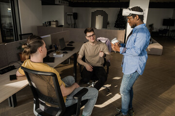 Fototapeta na wymiar IT Development Team Working on VR Project. Man wearing VR headset, playing and touching something in the virtual world. Diverse men programmers using VR technologies and computer to create video game.