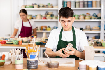 Fototapeta premium Young man in apron modeling clay pottery in workshop