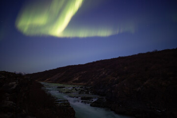 Aurora borealis winding over river valley, Iceland