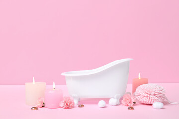 Small bathtub, burning candles, sponge, cotton balls and carnation flowers on color background