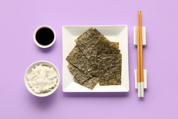 Plate with nori sheets, chopsticks, rice and soy sauce on color background