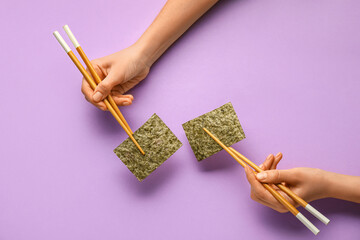 Woman holding chopsticks with nori sheets on color background © Pixel-Shot