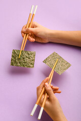 Woman holding chopsticks with nori sheets on color background
