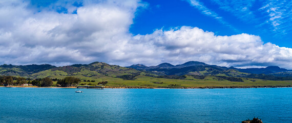 Panorama view of ocean with sailboat, hills, clouds, sea