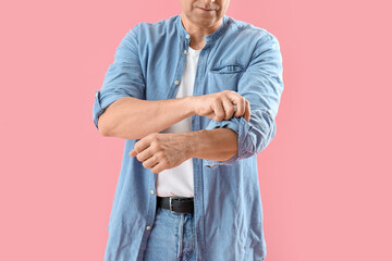 Mature man rolling up his sleeve on pink background, closeup