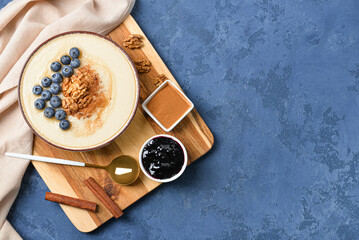 Bowl of tasty semolina porridge with blueberry, cinnamon, nuts and jam on color background