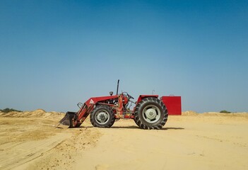 Red tractor on brown sand under blue sky