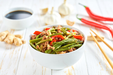 Traditional Chinese food, Szechuan style pork with green beans ginger and hot peppers on a white wooden table.