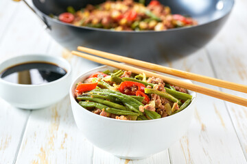 Fragrant spicy Chinese food minced ground pork belly stir fried with pickled yard long beans and red chili peppers on a wooden table.