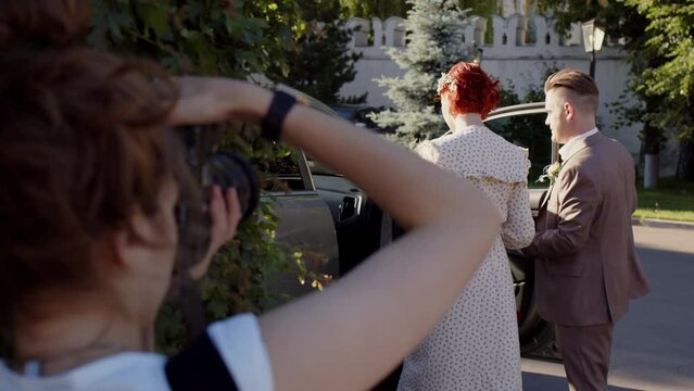 wedding photographer takes pictures of bride and groom getting into car. Photo session after wedding ceremony.