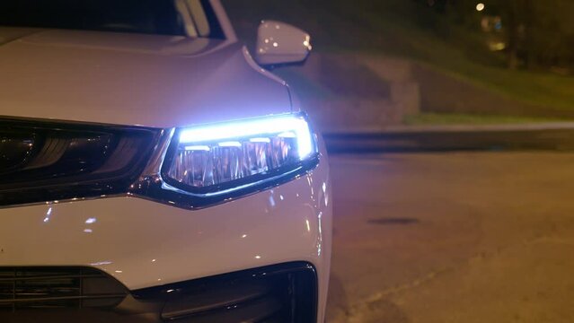 Close up view of headlight of car. modern diode front light of car parked on night street, cars passing nearby. gray small SUV