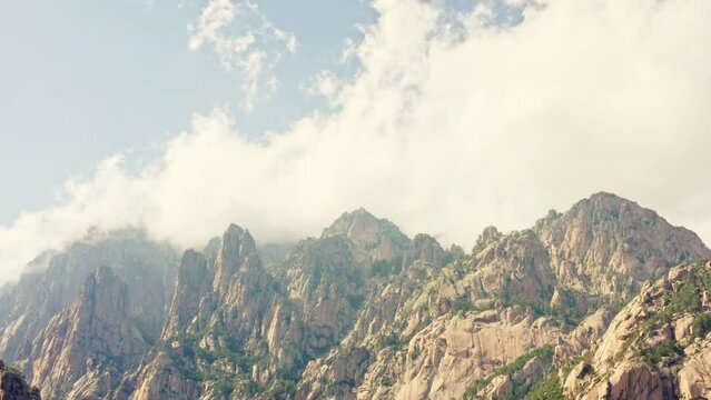 The aerial view of Aiguilles de Bavella in Corsica displays a striking landscape of rugged granite peaks, verdant forests, and winding rivers, creating a dramatic and picturesque natural scenery.