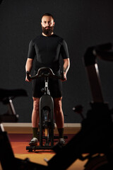 Fototapeta na wymiar Athlete training on an exercise bike. A man with a beard in sportswear pedals on an exercise bike