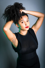 Beautiful young woman standing against gray background messing with her black hair.