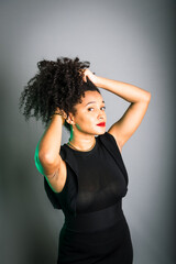 Beautiful young woman standing against gray background messing with her black hair.