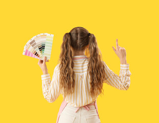 Female artist with paint color palettes pointing at something on yellow background, back view