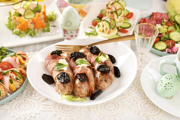 Easter white sausage wrapped in bacon with prune and salads on festive table