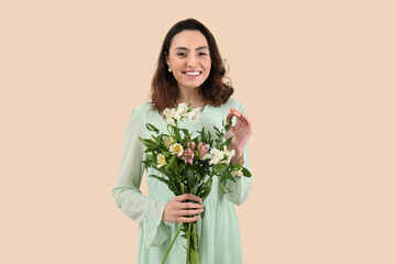 Young woman in dress with alstroemeria flowers on beige background