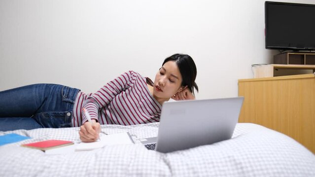 ベッドの横になって勉強する若い女性