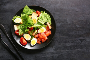 Plate of delicious salad with boiled eggs and salmon on black grunge background