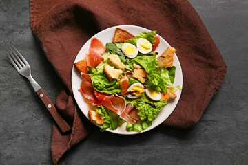 Plate of delicious salad with boiled eggs and jamon on black grunge background