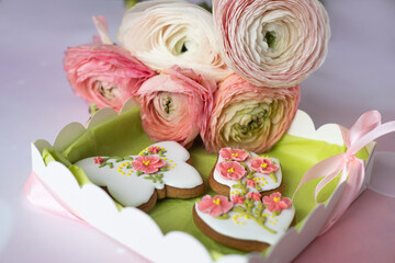 Handmade gingerbread butterfly and tulip in gift box next to bouquet of ranunculus asiaticus flowers on pink background. Beautiful gifts for Mother's day, March 8, birthday, Valentine's day. Postcard