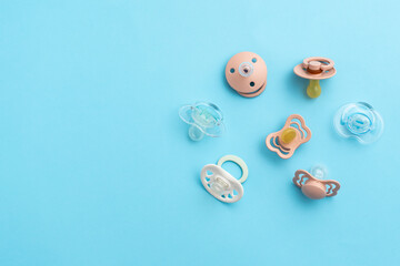 Many baby pacifiers on blue background with copy space, top view of soothers, flat lay