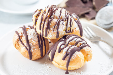 Profiteroles with whipped cream and chocolate filling, covered with melted chocolate, horizontal closeup