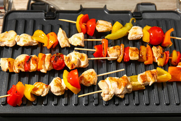 Modern electric grill with tasty chicken skewers and vegetables on table