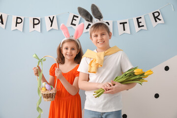 Little children in bunny ears with Easter eggs and tulips at home