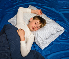 Young sleeping preteen boy in pajamas laying in bed with pillow