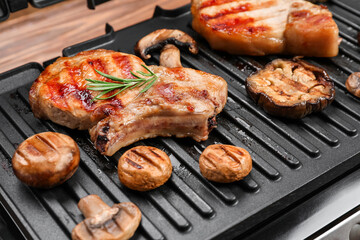 Modern electric grill with tasty steaks and vegetables on table, closeup