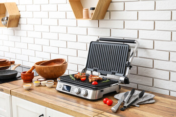 Modern electric grill with tasty steaks on table near white brick wall