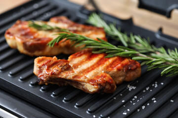 Modern electric grill with tasty steaks on table, closeup